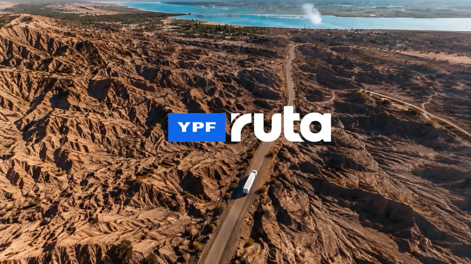 Vista aérea de un camión circulando por una ruta entre cañadones, con el logo de YPF RUTA sobreimpreso